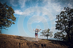 An attractive blonde girl in striped shorts and a blue t-shirt stands on the hills