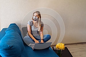 Attractive blonde girl wearing a protective mask works hard and responsibly with a laptop remotely at home. Isolated due to the