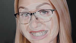 Attractive blonde hair business woman in glasses is looking at camera and smiles to show teeth braces standing at black