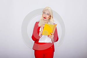 Attractive blonde haired woman wearing red jacket and pants, holding book in her hands