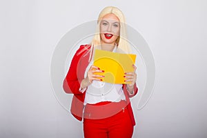 Attractive blonde haired woman wearing red jacket and pants, holding book in her hands