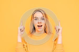 Attractive blonde with a shocking face is isolated on a yellow background, looks at the camera with astonishment and shows fingers