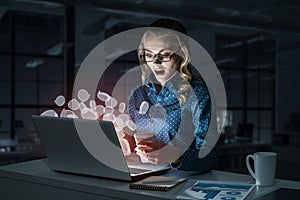 Attractive blonde wearing glasses in dark office using laptop. M