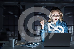 Attractive blonde wearing glasses in dark office using laptop. M