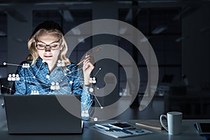 Attractive blonde wearing glasses in dark office using laptop. M