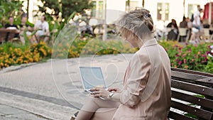 Attractive blonde white woman working freelance with laptop and smartphone in park at sunny day