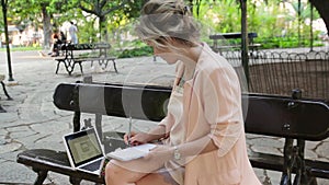 Attractive blonde white woman working freelance with laptop and smartphone in park at sunny day