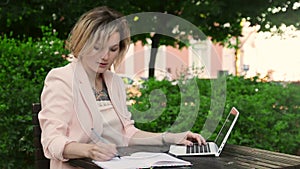 Attractive blonde white woman working freelance with laptop and smartphone in park at sunny day