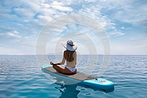 Blonde woman relaxes in a yoga position on a stand up paddle board SUP