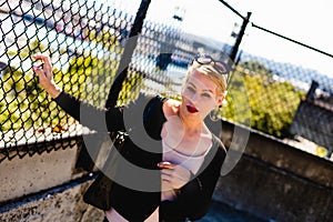 Attractive blonde woman standing on a city sidewalk next to a fence