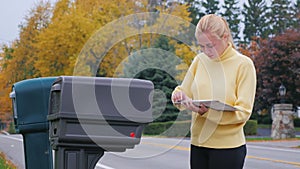 Attractive blonde woman takes the mail from the mailbox. Countryside in USA