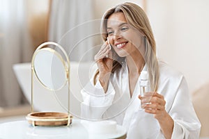 Attractive blonde woman using face tonner, looking at mirror