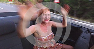 Attractive blonde woman waving her arms to music riding in convertible car