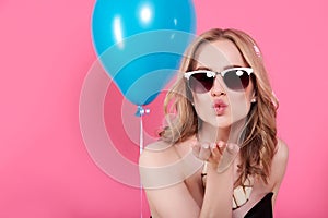 Attractive blonde young woman in elegant party dress and golden jewelry celebrating birthday and blowing a kiss towards camera.