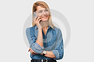 Attractive blonde young woman talking on mobile phone to her friend, looking cheerful and happy, posing on white studio background