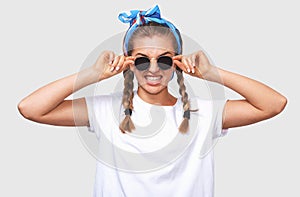 Attractive blonde young woman wearing trendy sunglasses, white t-shirt and blue headband, smiling broadly. Student girl going