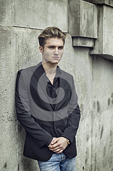 Attractive blue eyed, blond young man leaning against white wall