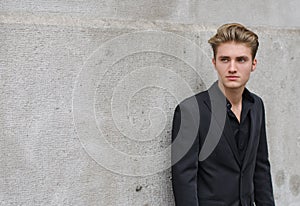 Attractive blue eyed, blond young man leaning with his back against wall