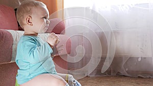 An attractive boy 2 years old sits on a pot at home and eats a banana. Looks closely at the TV.