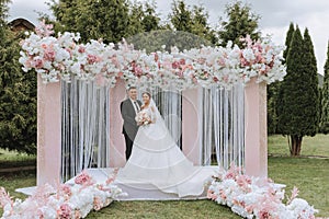 Attractive bride and groom at the ceremony on their wedding day with an arch made of pink and white flowers