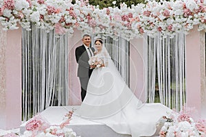 Attractive bride and groom at the ceremony on their wedding day with an arch made of pink and white flowers