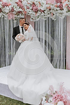 Attractive bride and groom at the ceremony on their wedding day with an arch made of pink and white flowers