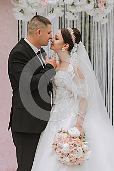 Attractive bride and groom at the ceremony on their wedding day with an arch made of pink and white flowers