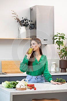 An attractive brunette drinks a green smoothie in her kitchen. The concept of healthy nutrition, detox.