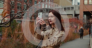 Attractive brunette female taking pictures filming video using smartphone in autumnal High Line Park in New York