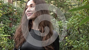 Attractive brunette girl in black dress walking through tropical plants in greenhouse. 4K clip