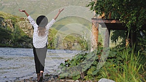 Attractive brunette in a hat and a white shirt in peas enjoys nature in the mountains. Young woman tourist walks along