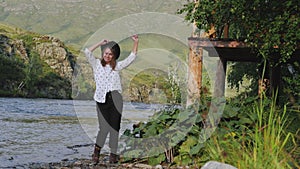 Attractive brunette in a hat and a white shirt in peas enjoys nature in the mountains. Young woman tourist walks along