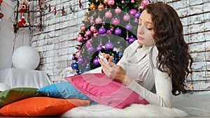 Attractive brunette lying on bright pillows near the Christmas tree and listening to music. Unconventional Christmas