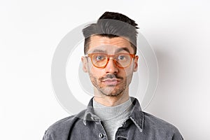 Attractive brunette man with moustache, wearing stylish glasses and look serious at camera, no emotion pokerface