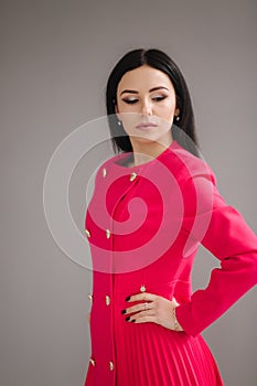 Attractive brunette model in crimson dress on gray background in studio