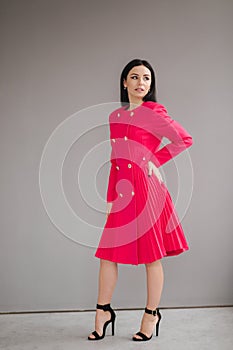 Attractive brunette model in crimson dress on gray background in studio