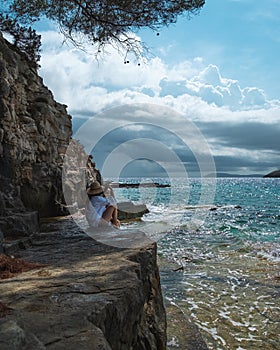 Attractive brunette sitting on a rock on the shores of the Adriatic sea , island of Vis in Croatia. Cloudy summer day, beautiful