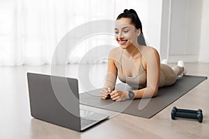 Attractive brunette sporty woman exercising at home, using laptop