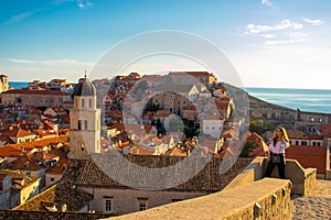 Attractive brunette standing on the city walls of the old town of Dubrovnik, small houses and rooftops surrounding the whole
