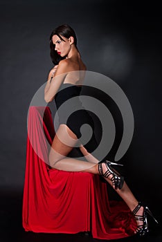 Attractive brunette wear black dress kneeling on chair covered with red fabric