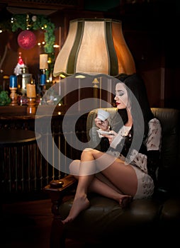 Attractive brunette in white comfortable blouse holding a cup of coffee. Portrait of sensual woman in classic boudoir scene.