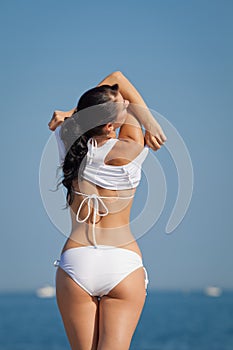 Attractive brunette in white swimwear undressing on the beach