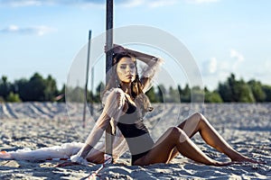 Attractive brunette woman in black body and translucent beach cover up posing on sandy beach at sunset. sitting and looking at