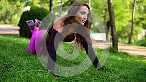 Attractive brunette woman doing push up workout exercise on the grass in the park. Push ups with knees. Slowmotion shot