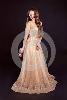 Attractive brunette woman in golden long dress isolated on black