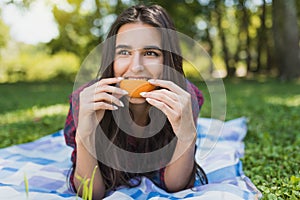 Attractive brunette woman lying on green grass in outdoor eating orange fruit, copy space for your advertising message or content