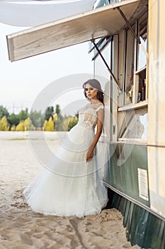 Attractive brunette woman with makeup and hairstyle wearing white wedding dress while posing and lean near street food car.