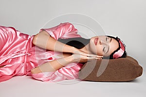 Attractive brunette woman in pink gown is laying on pillow with eyes closed on floor with blindfold