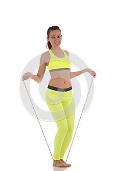 Attractive brunette woman in sports neon yellow bra and leggings doing exercises using a long skipping-rope.