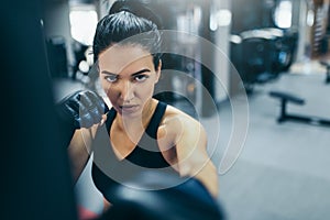 Attractive brunette woman trainer punching a bag with kickboxing gloves in the gym and looking front at the camera. Sport, fitness